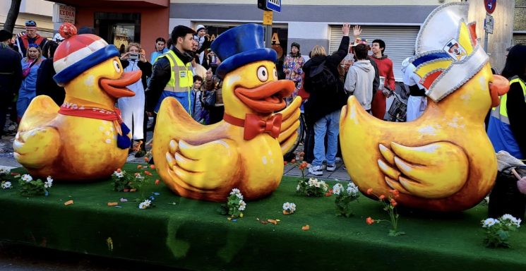 Drei große, bunte Enten mit Hüten auf einer Veranstaltung, umgeben von Menschen.